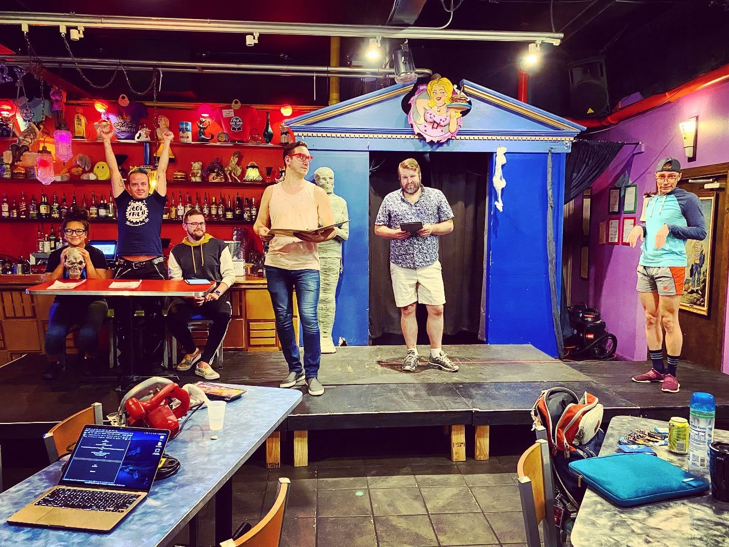 Company members rehearse with scripts on a small stage.